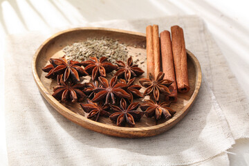 Wooden plate with anise stars, seeds and cinnamon on white background