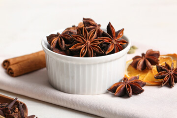 Bowl with anise stars, cinnamon and slice of dried orange on white wooden background
