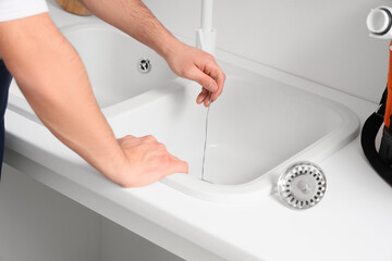 Male plumber with wire clearing drain in kitchen, closeup © Pixel-Shot
