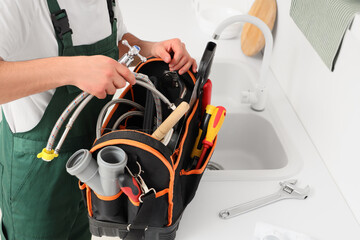 Male plumber with tool bag near sink in kitchen, closeup