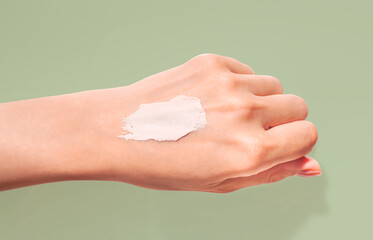 Cosmetic texture white creamy swatch on woman hand green sage background