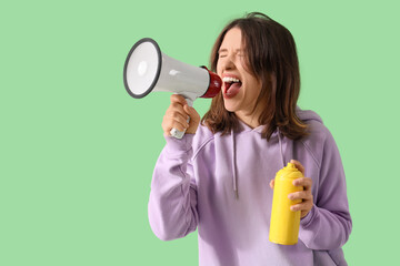 Young woman with paint spray can shouting into megaphone on green background. Artist as Outlaw Day