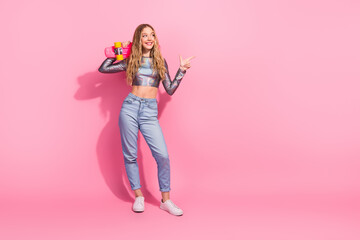 Trendy young woman in metallic top holding skateboard on vibrant pink background