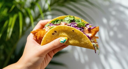 Hand holding fish taco garnished with vegetables and herbs