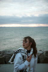 Fototapeta premium Beautiful young girl in a white tracksuit stands on the seashore in stormy weather