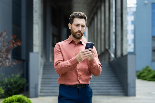 Serious thoughtful man thinks while reading emails, businessman walks with smartphone in hands uses messaging app.