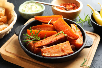 Pieces of tasty cooked sweet potato with rosemary in baking dish served on grey textured table, closeup