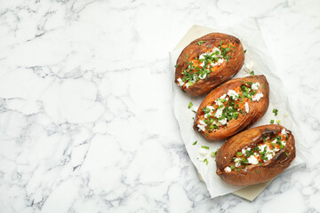 Tasty cooked sweet potatoes with feta cheese, green onion and parsley on white marble table, top view. Space for text