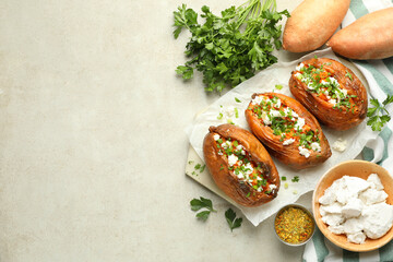 Tasty cooked sweet potatoes with feta cheese, green onion and parsley on gray textured table, flat lay. Space for text