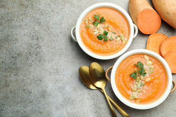 Delicious sweet potato soup with pumpkin seeds in bowls and fresh vegetables on grey textured table, flat lay. Space for text