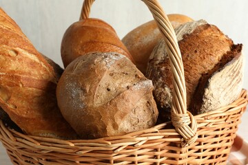 Different freshly baked bread loafs in wicker basket on table, closeup