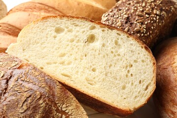 Whole and cut bread loafs on white table, closeup