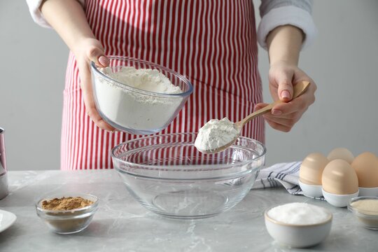 Making cinnamon rolls. Woman adding flour into bowl at gray marble table, closeup