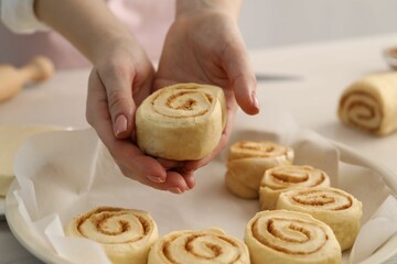 Woman putting cinnamon roll into baking dish at table, closeup