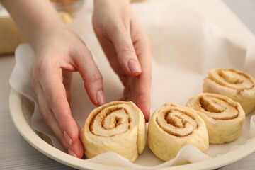 Woman putting cinnamon roll into baking dish at table, closeup