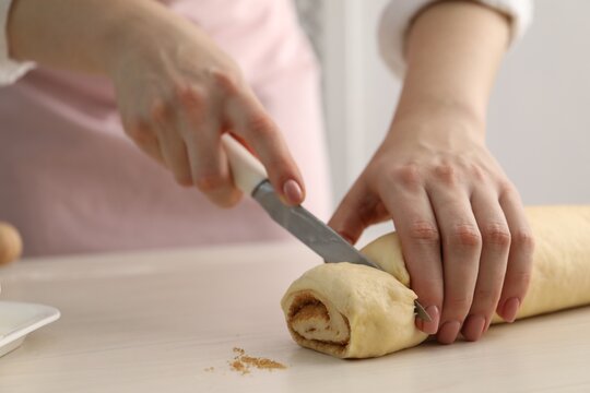 Making cinnamon rolls. Woman cutting dough at white wooden table, closeup