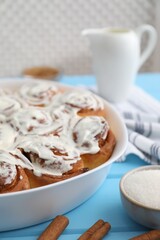 Delicious frosted cinnamon rolls in baking dish on light blue wooden table, closeup