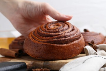 Woman with delicious cinnamon roll bun at table, closeup
