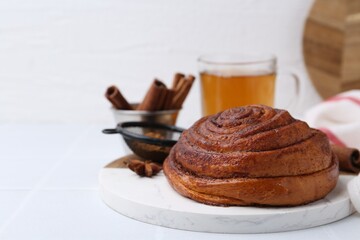 Delicious cinnamon roll bun, tea and spices on white table, closeup. Space for text