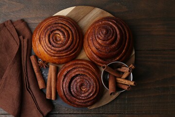 Delicious cinnamon roll buns and spices on wooden table, top view