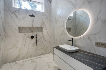 Stylish bathroom design with a small window. Black shower watering can. Round mirror with backlight...