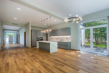 A large room of a private house with a panoramic window. Laminated floor. Part of the room is occupied by a kitchen set.