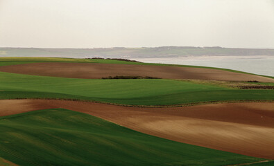Green and brown rolling hills with farmland near the coastline of Europe, France. Concept of nature, agriculture, and the serene beauty of rural landscapes.