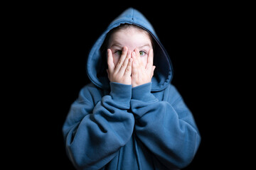 Girl in blue hoodie in the dark covering her face with her hands. Concept of kidnapping, fear,...