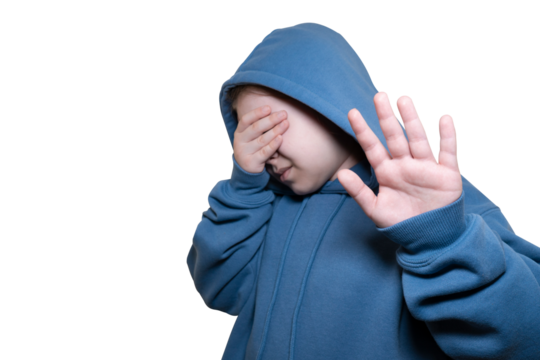 Girl dressed in blue hoodie covers her face with her hand on green background (chroma key). Concept of kidnapping, fear, fright and loneliness