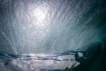 An underwater view of a powerful wave curling and capturing light, highlighting the raw energy and...