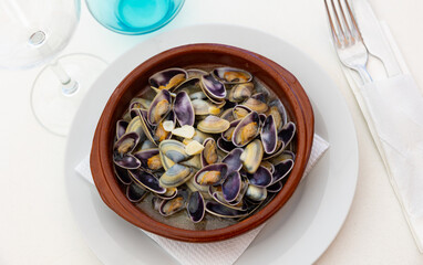 Gourmet Mediterranean seafood tapas. Delicious steam cooked clams in flavorful garlic broth served in clay bowl