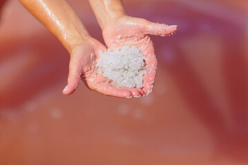 A close-up of hands gently cradling a mound of glistening salt crystals from the pink waters of a salt lake, with water droplets shining in the sunlight for a tranquil effect.