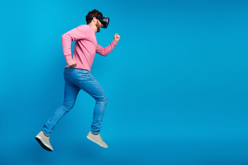 Brunet man experiencing virtual reality while jumping in casual wear against a vibrant blue background