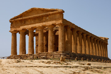 Obraz premium A breathtaking view of Valle dei Templi in Sicily, Italy, featuring ancient Greek temples surrounded by lush greenery and dramatic skies, showcasing the timeless beauty of historical architecture.