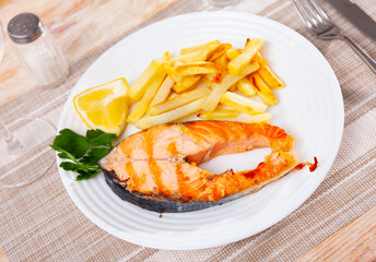 Delicious homemade dinner of baked salmon steak and fried potatoes served with lemon garnished with greens..