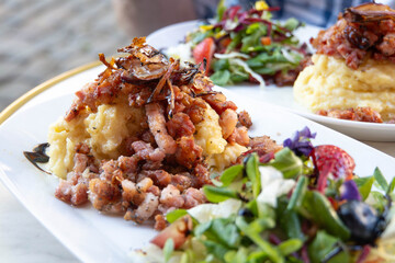 Traditional Danish dish - Burning love (Brændende kærlighed) consisting of mashed potatoes topped with fried bacon and onions, with a berry and flower salad on a white plate