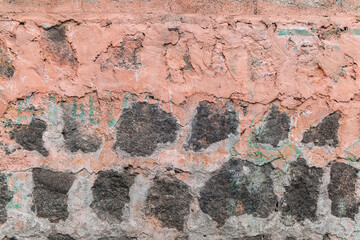 Pink stucco partially covering a stone wall.