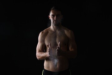 Fototapeta premium Man clapping hands with talcum powder before training on black background