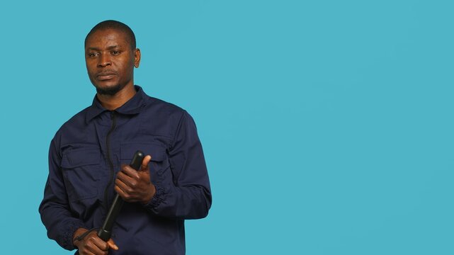Portrait of security staff member tasked with evicting trespassers, intimidating them with baton. Patrolling agent maintains secure environment using truncheon weapon, studio background, camera A