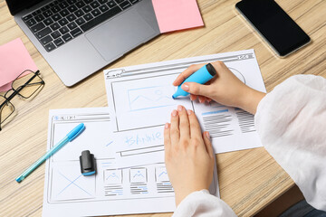 Website designer creating wireframe on paper with highlighter at wooden table, above view