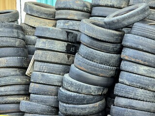 A large pile of old, used car tires stacked together, showcasing patterns and textures of worn...