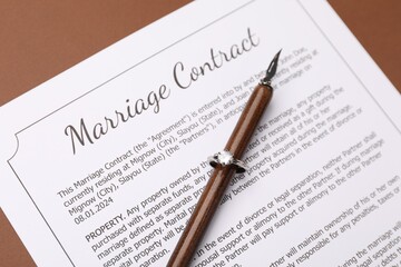 Fototapeta premium Marriage contract, pen and ring on brown background, above view