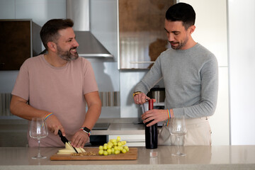 two lgtbi couple boys in the kitchen of their house preparing an appetizer while drinking wine