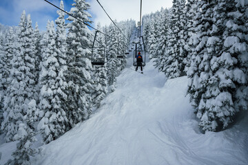 Snowboarder riding a chairlift through the snow covered mountains of Steamboat Springs Colorado