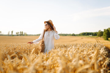Naklejka premium Young beautiful woman in golden wheat field. Concept of summer, freedom, warmth, harvest, recreation, agriculture.