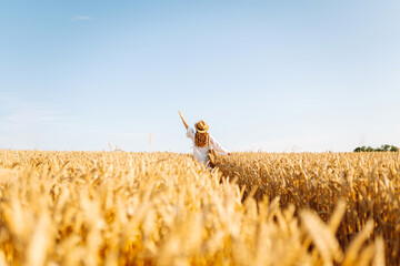 Young beautiful woman in golden wheat field. Concept of summer, freedom, warmth, harvest, recreation, agriculture.