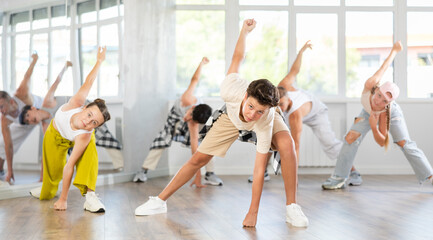 Team of positive teenagers rehearsing modern dances in dance hall