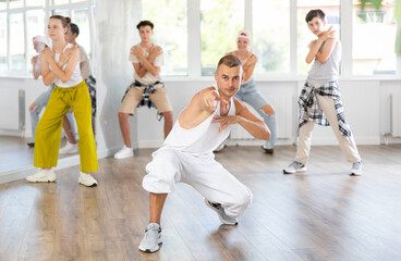 Fototapeta premium Young male teacher dancing hip hop dance with group of teenagers in studio