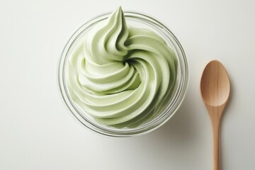 A glass bowl of swirled light green matcha frozen yogurt, a wooden spoon rests beside it.