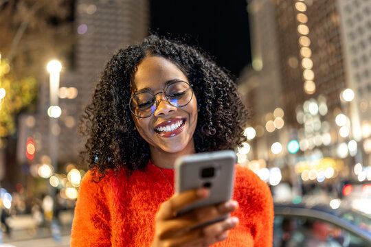 Young woman using smartphone on city street at night